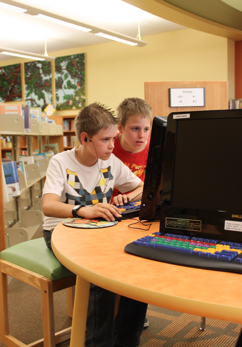 Two tween boys playing on desktop computer in library