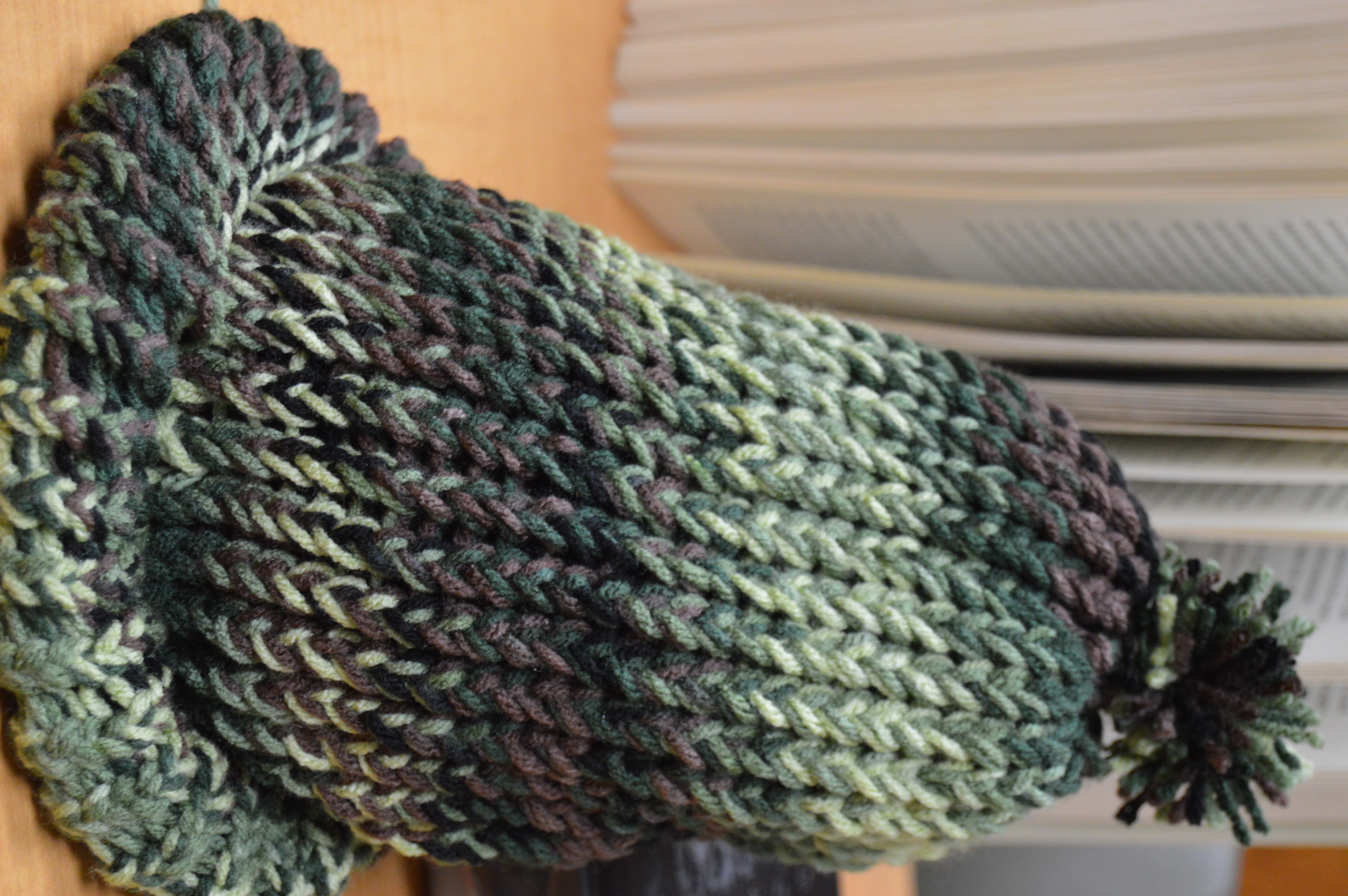 picture of a green camouflage loom knitted hat with a little pompom on top.