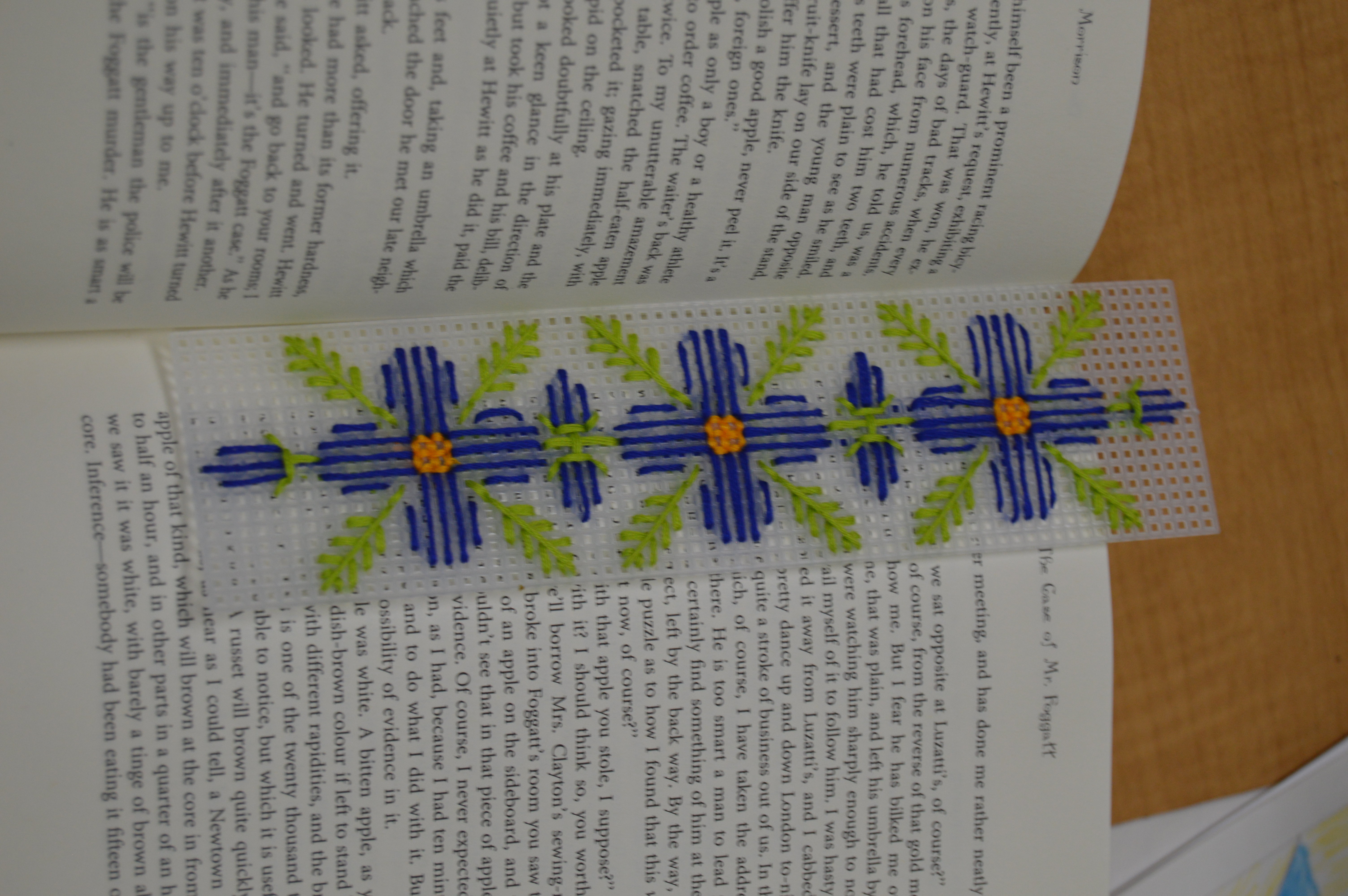 picture of a book with a plastic canvas bookmark with blue flowers on it in a book.