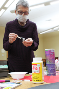 Baxter County Library volunteer Suzanne Sutherland glues pieces in preparation for the kids piggy bank craft class